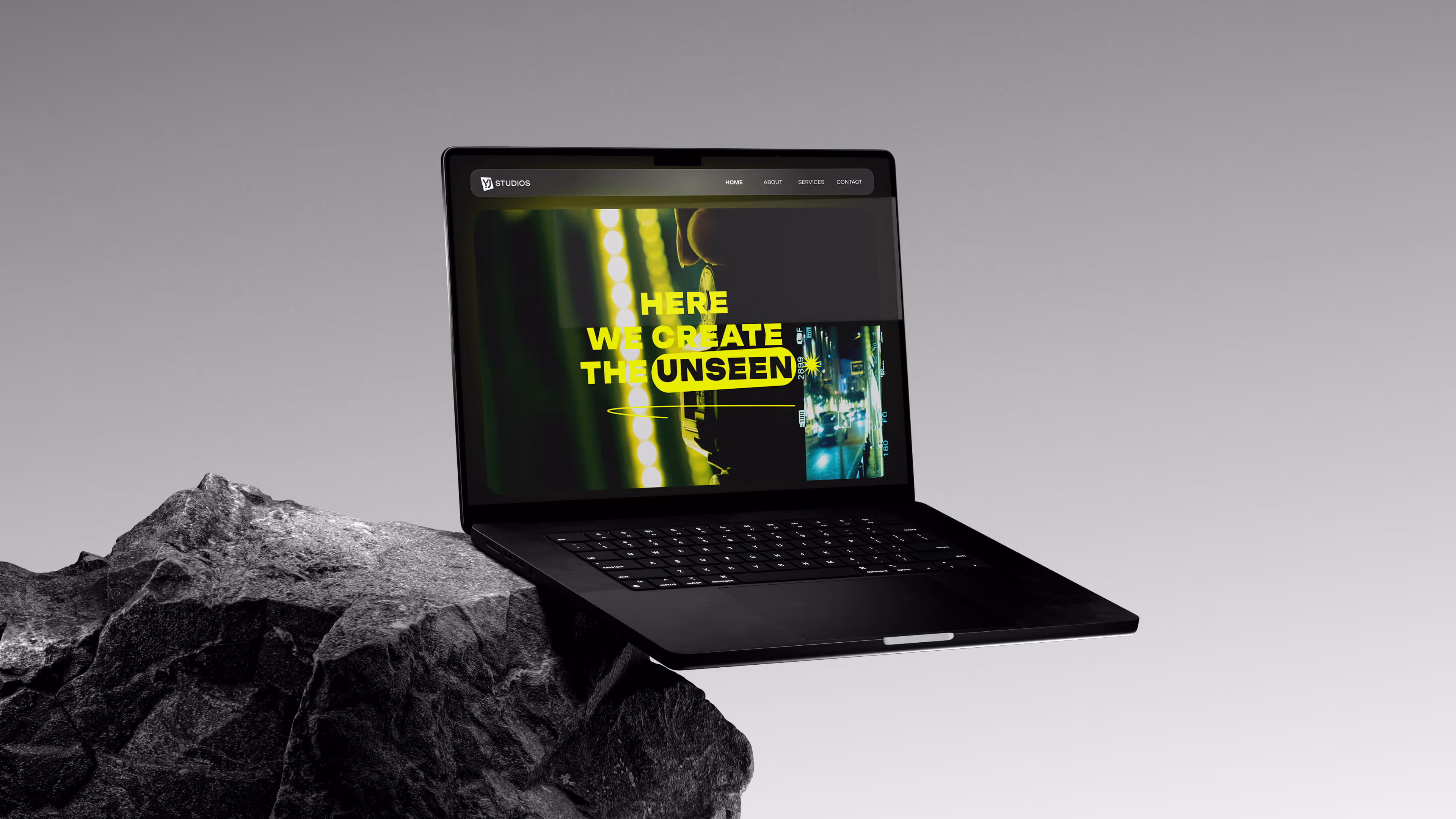 Black laptop on a rock showing webpage with yellow text: Here we create the unseen.