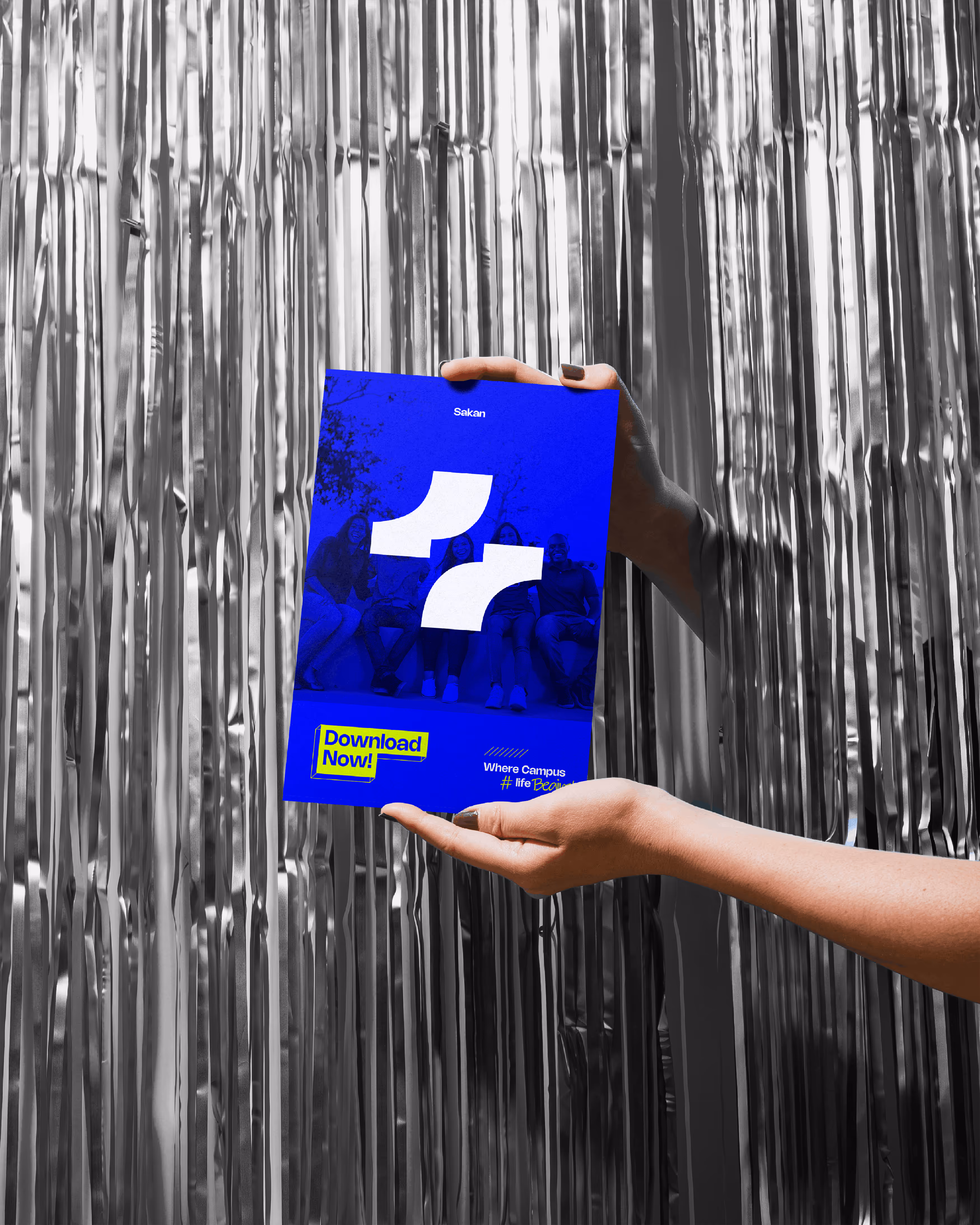 Two hands hold a blue poster with white shapes, text, and a group of people faintly visible.