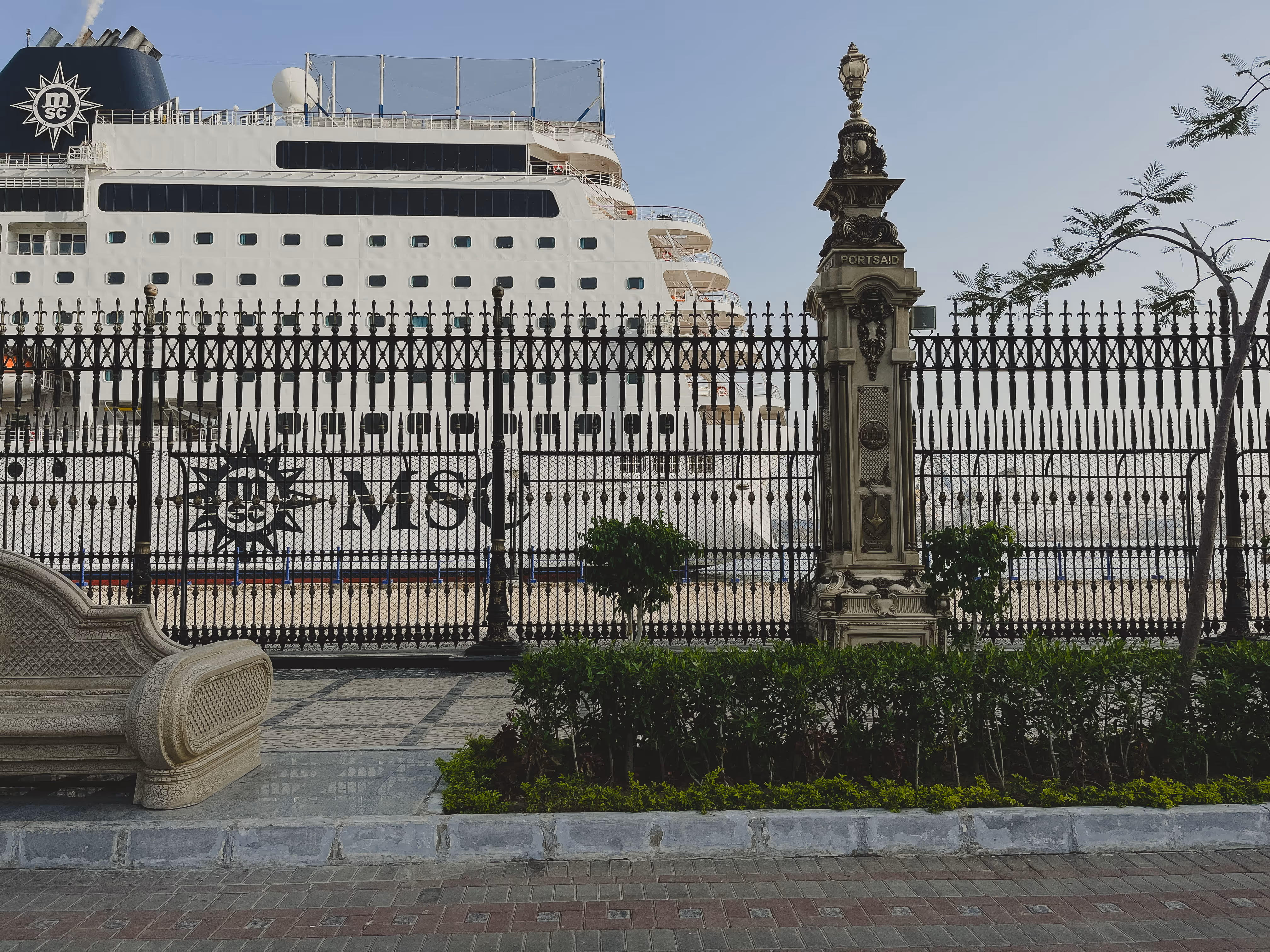 Large white MSC cruise ship docked behind decorative iron fence with PORT SAID pillar outside.