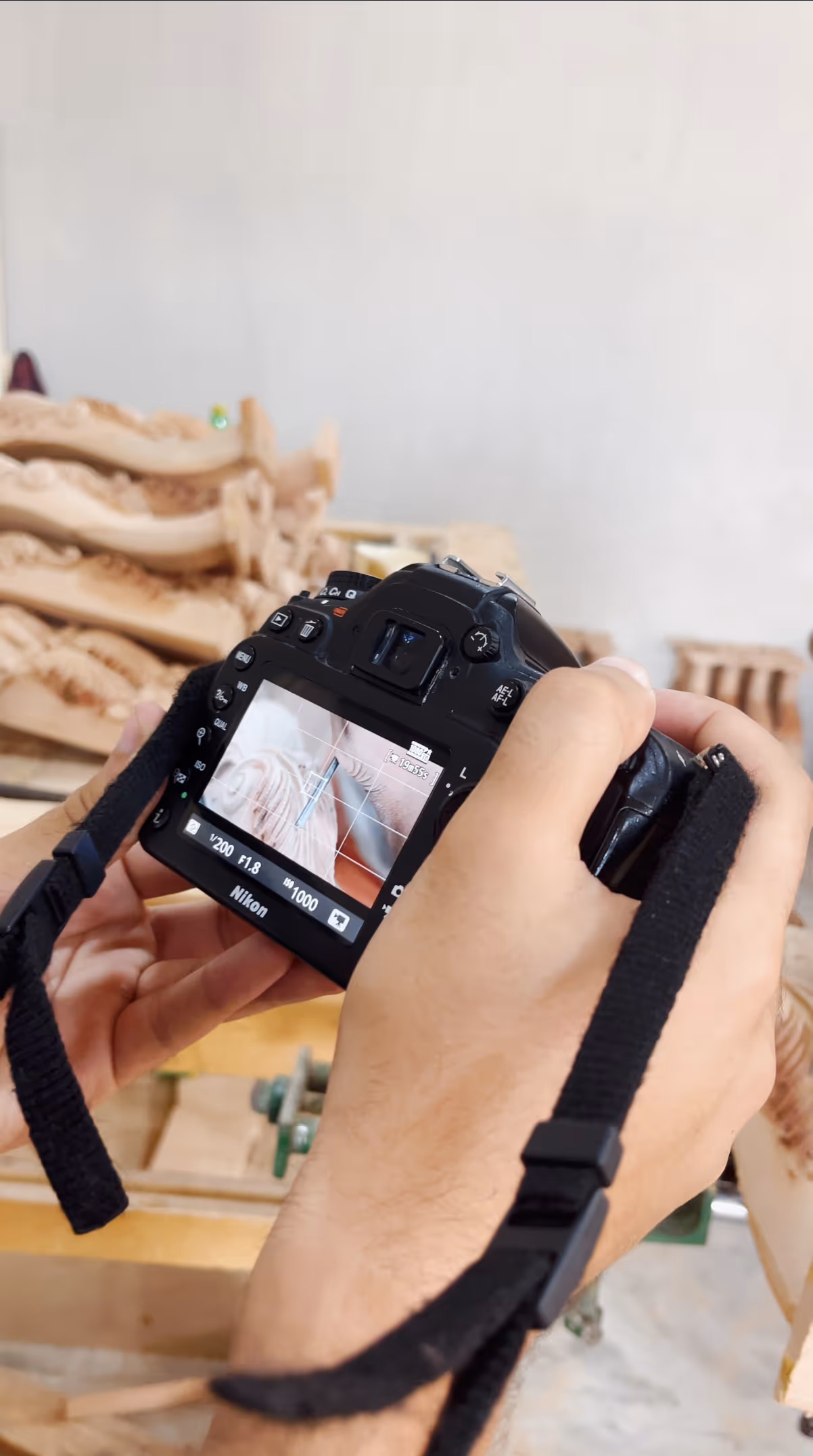 Hands holding Nikon DSLR camera showing focus on wood carving details on screen.