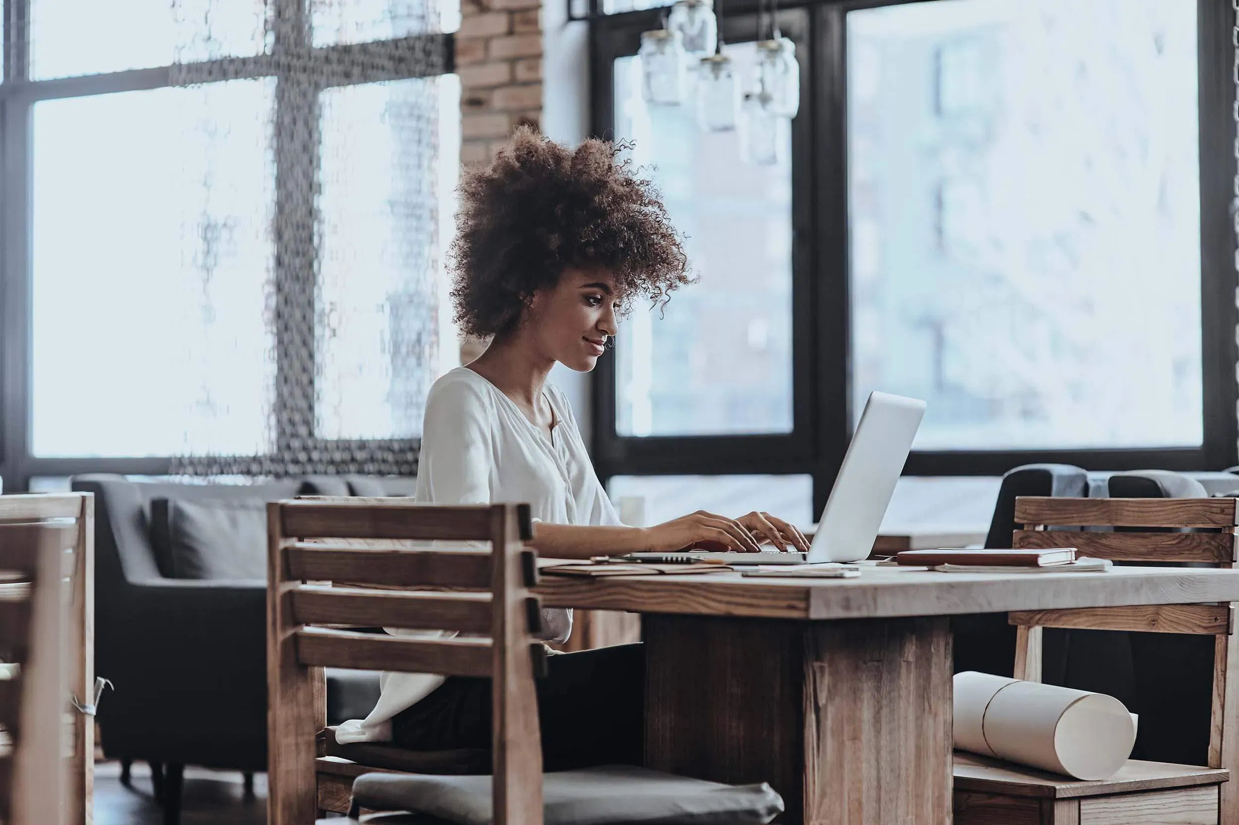 A woman works on her laptop at a wooden table in a bright, modern home setting, representing remote work capability.