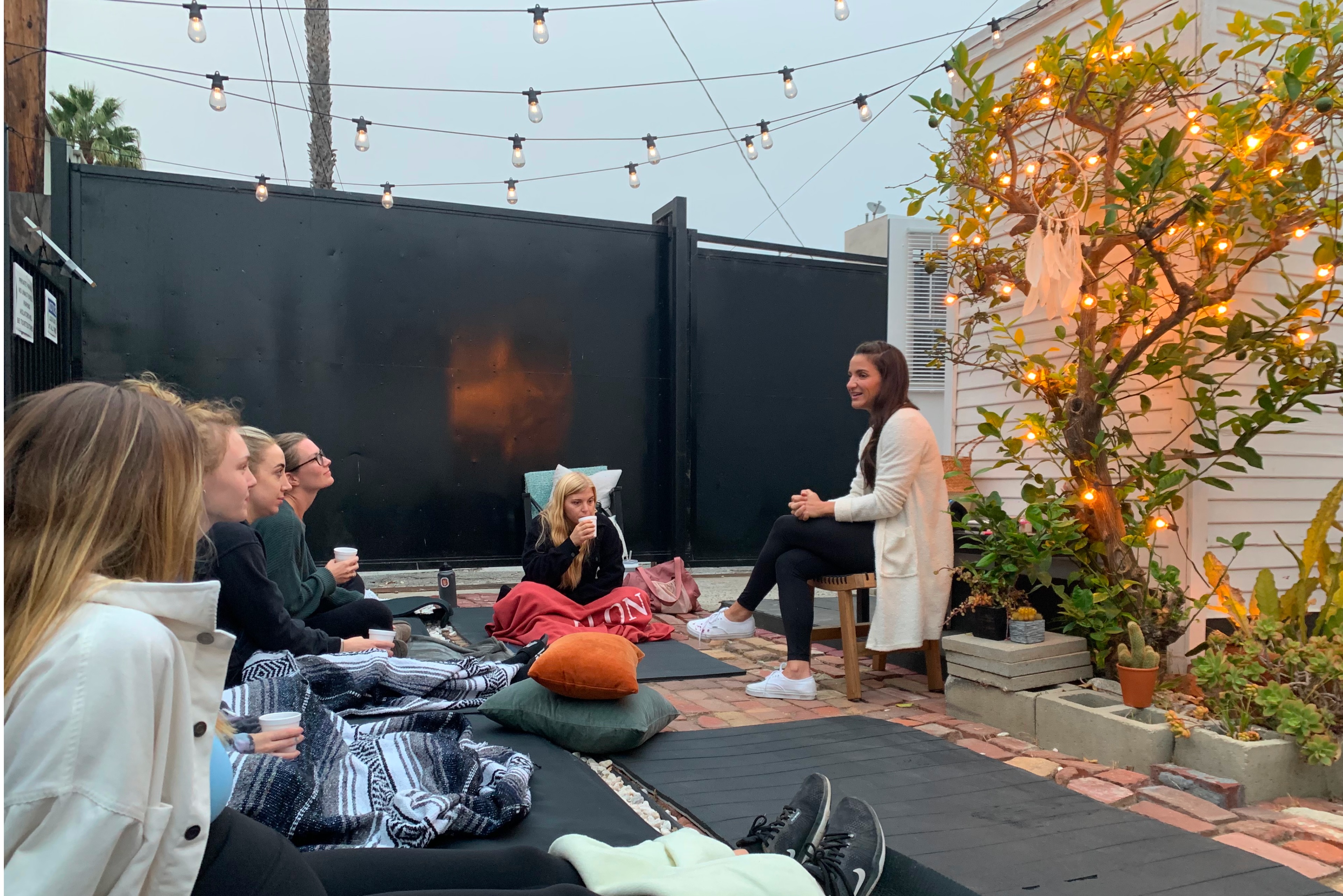 Annie leading a small evening breathwork circle on a Venice patio under string lights.