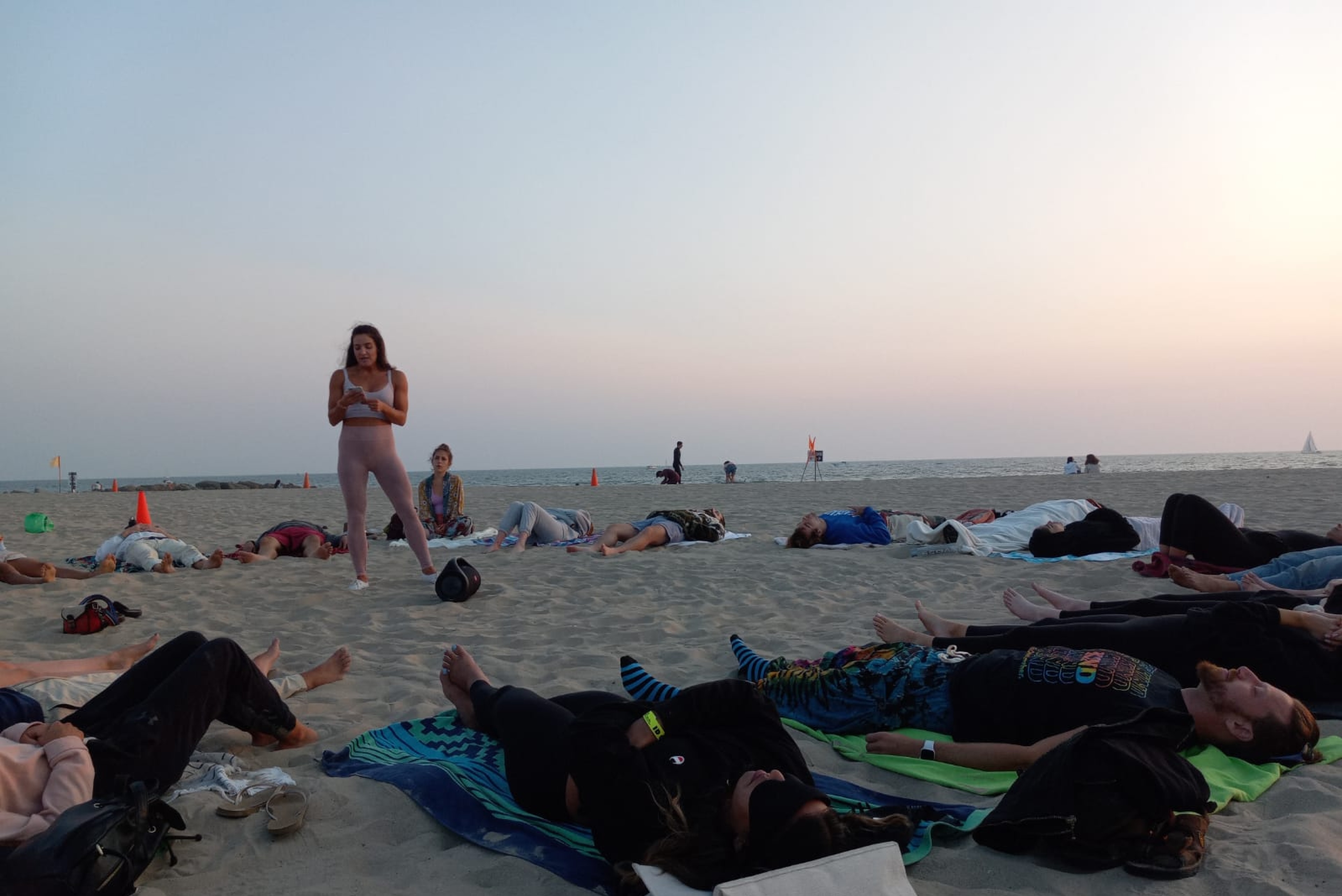 A large group lying on towels at dusk during a beach breathwork session in Venice.