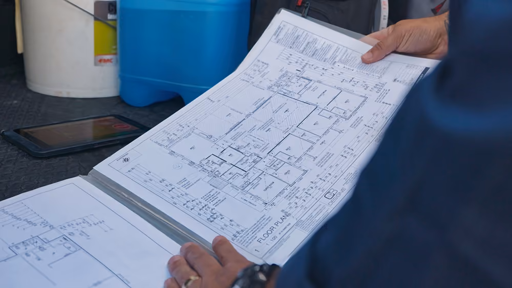 Person holding an architectural floor plan sheet showing a house layout with rooms and measurements.