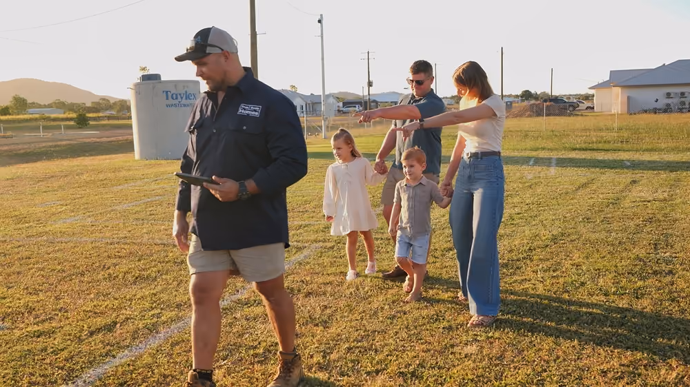 Man in uniform leads a family of four across a grassy field in late afternoon sunlight.