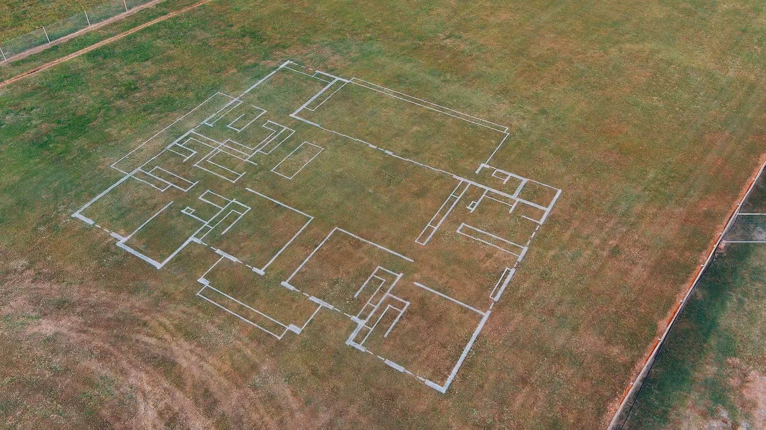 White foundation lines of a house layout marked on an empty grass field from above.