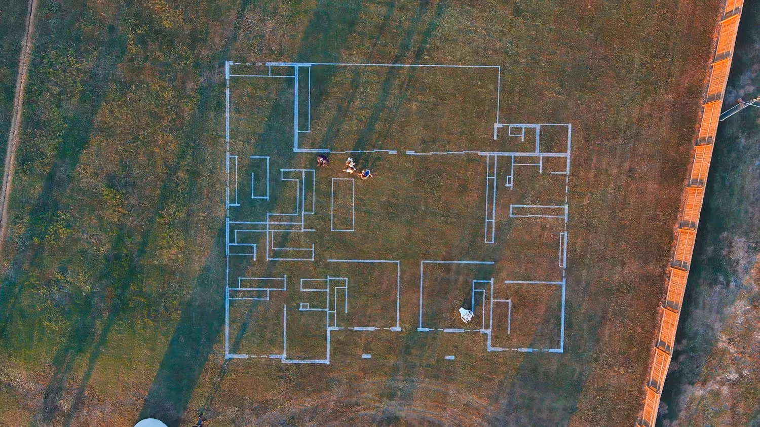 Aerial view of a house floor plan outlined on grass with four people standing inside the layout.