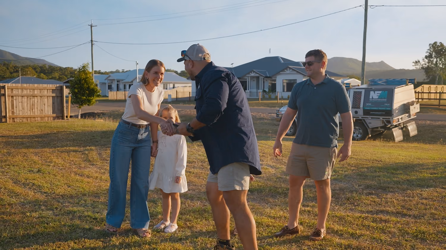 Two men and a woman shake hands outdoors with a little girl standing beside the woman.
