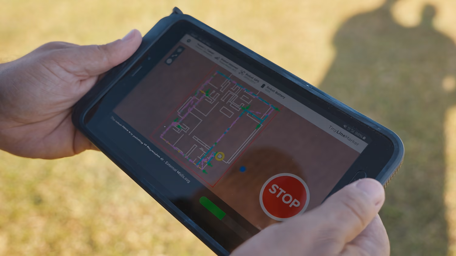 Hands holding a tablet showing a house floor plan with a red stop button on the screen.