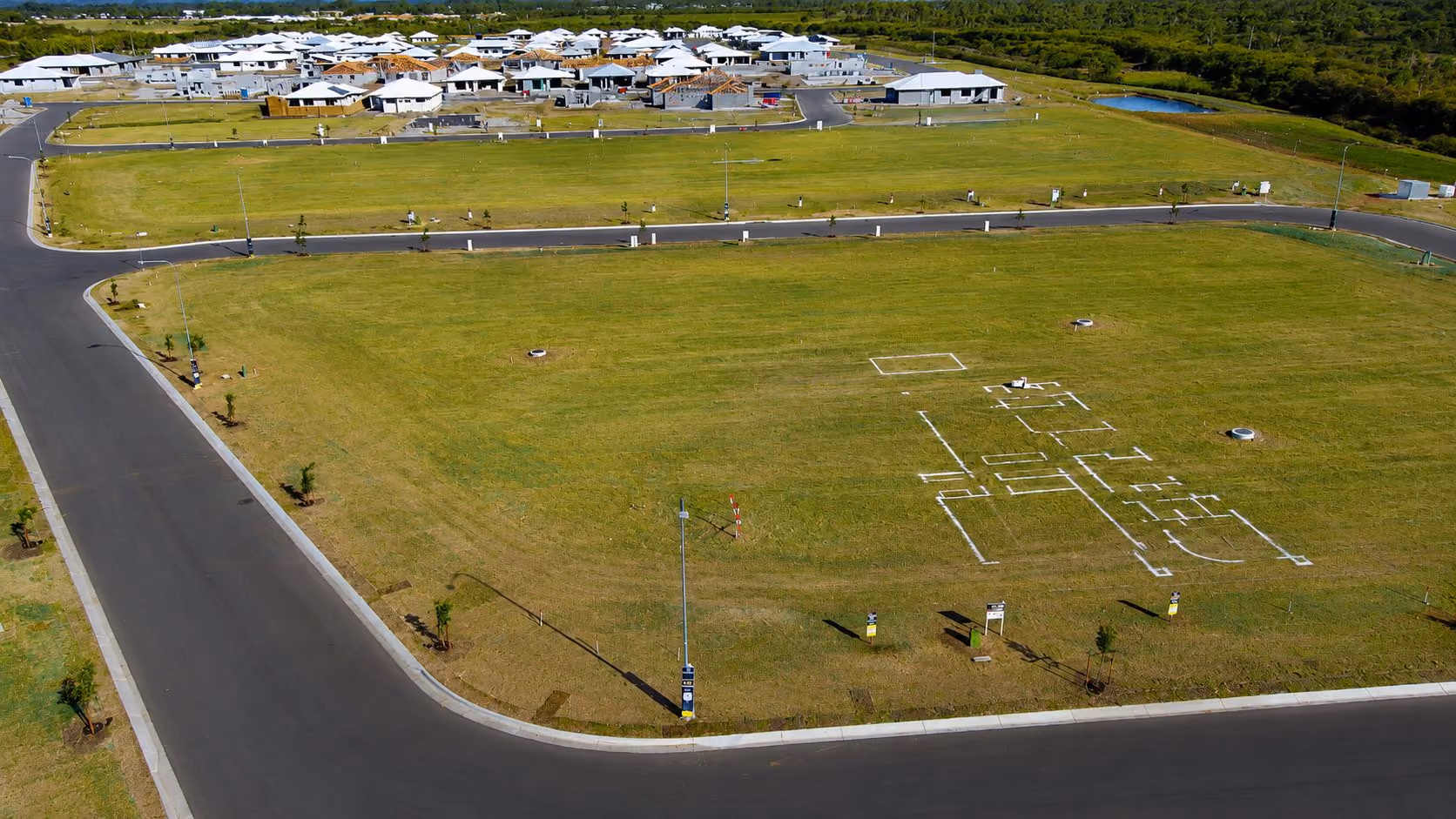 Aerial view of a residential development with empty grassy lots and foundation outlines for new homes.