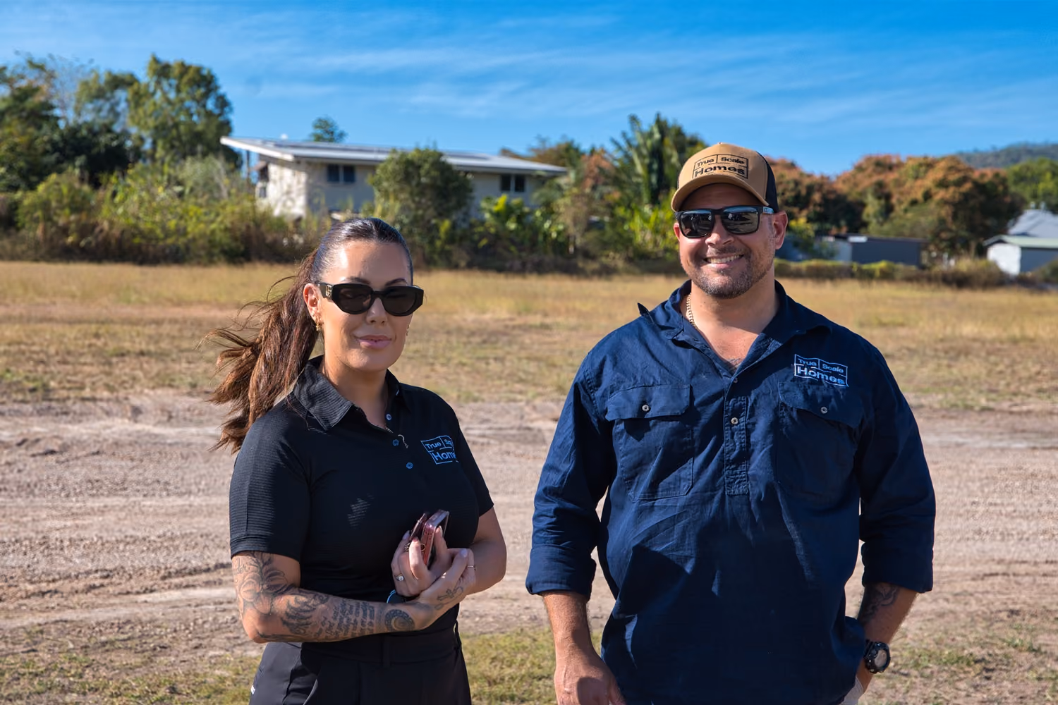 Man and woman outdoors wearing True Scale Homes shirts and sunglasses on a sunny day.