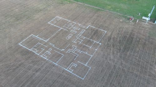 Large residential house floor plan outlined with white paint on a brown grassy field.