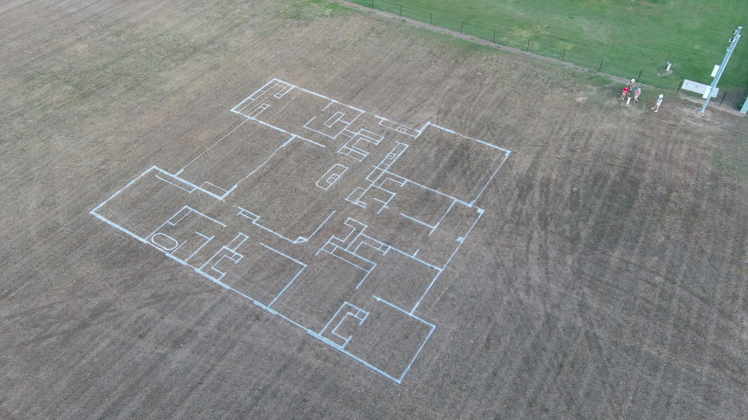 Large residential house floor plan outlined with white paint on a brown grassy field.