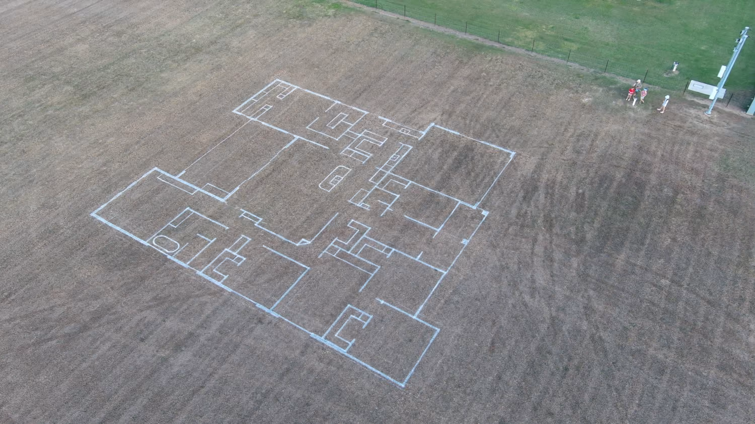 Large residential house floor plan outlined with white paint on a brown grassy field.