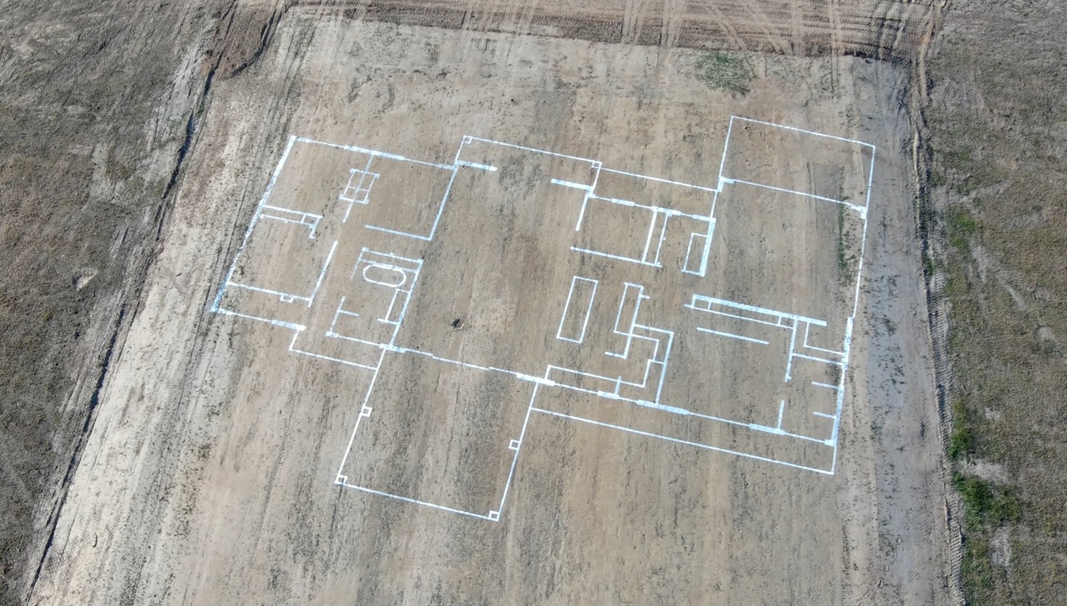 White outline of a house floor plan marked on a cleared dirt plot ready for construction.