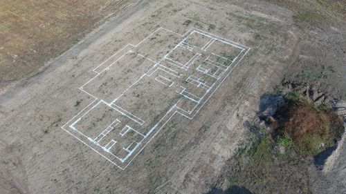 Aerial view of a building foundation layout marked with white lines on bare ground.