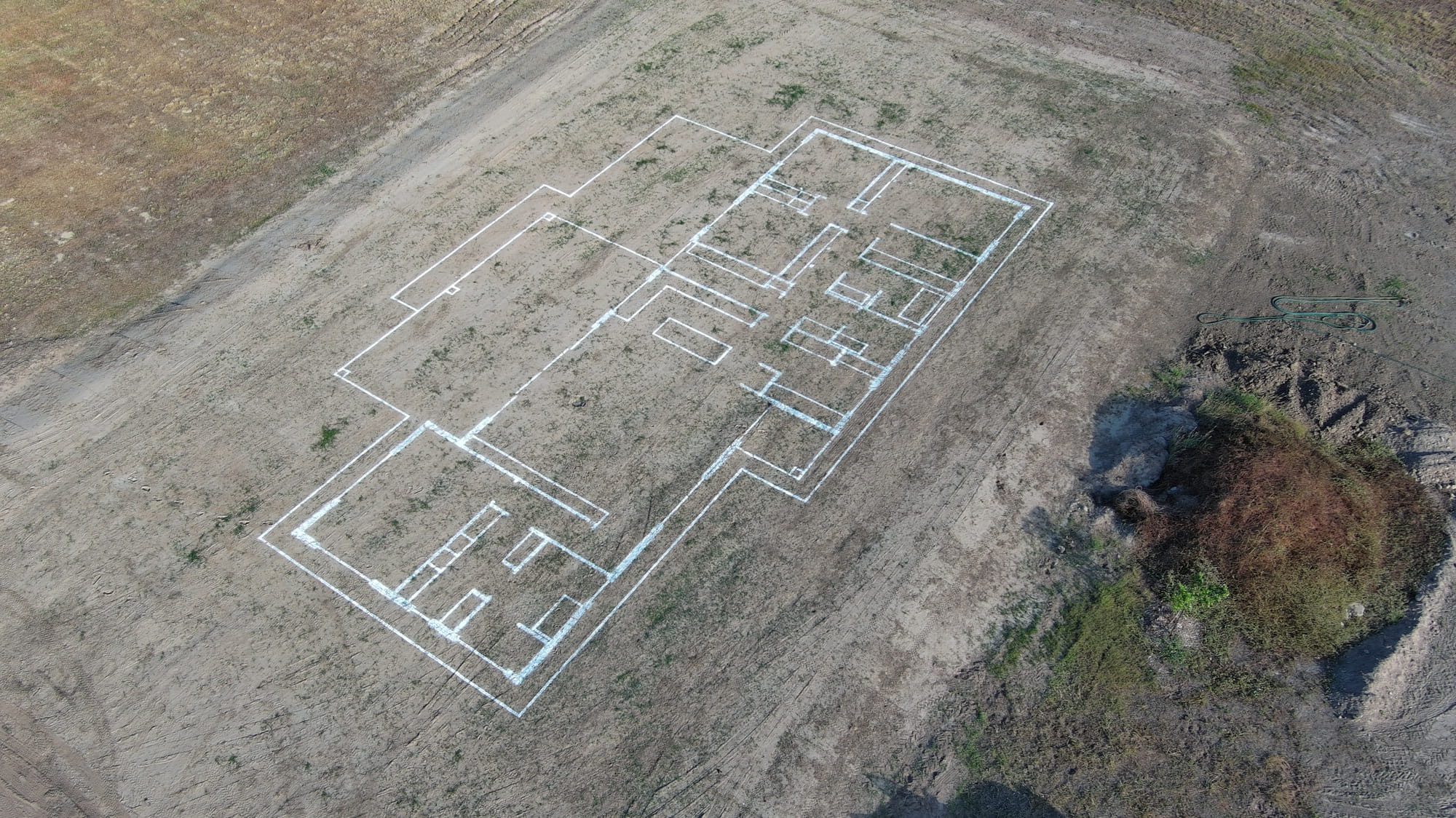 Aerial view of a building foundation layout marked with white lines on bare ground.