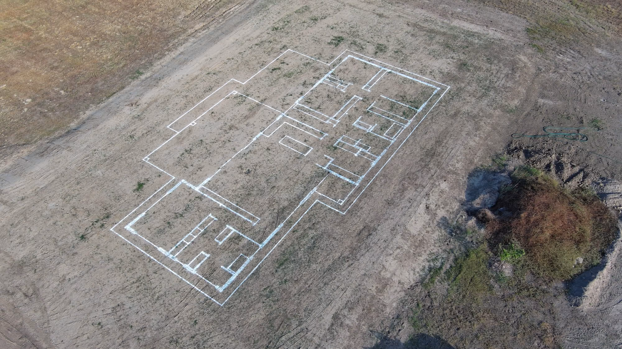 Aerial view of a building foundation layout marked with white lines on bare ground.
