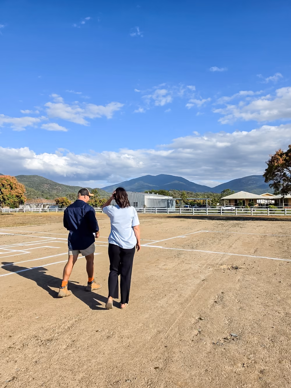 People walking through a marked full-scale house layout with mountains in the background.