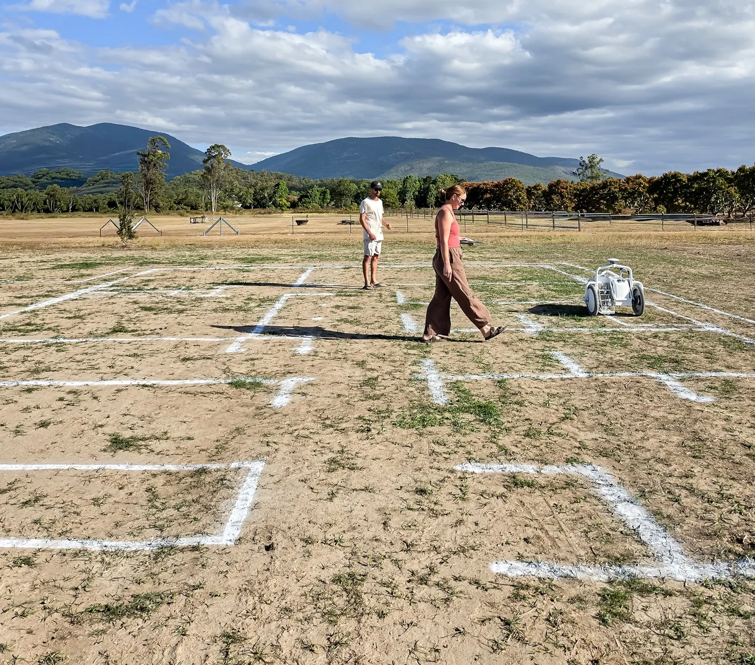 People walking through a full-scale house layout on a rural block with mountains in the background.
