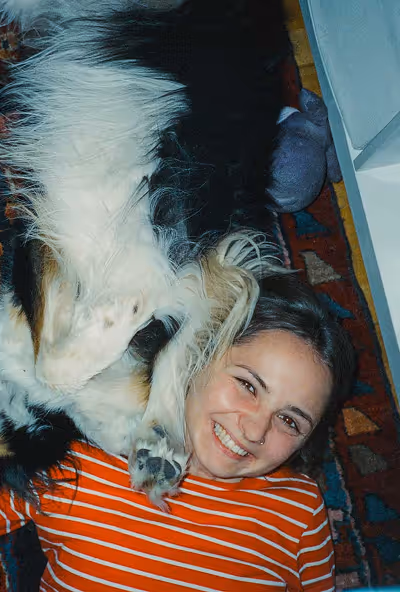 Smiling woman lying on a patterned rug with a large black and white dog resting its head close to hers.