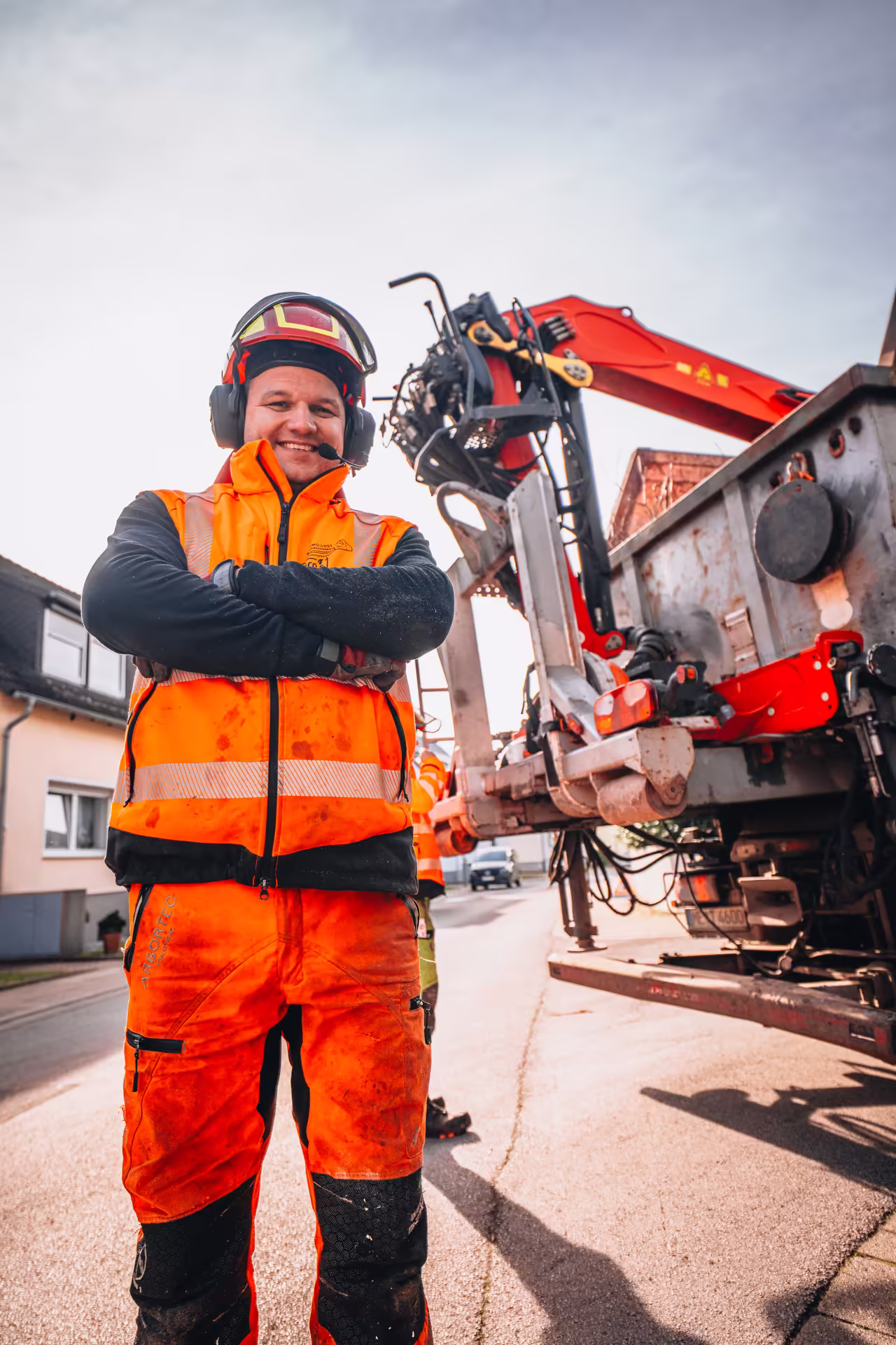 Lächelnder Arbeiter in orangefarbener Schutzkleidung vor einer Fahrzeugmaschine auf der Straße.