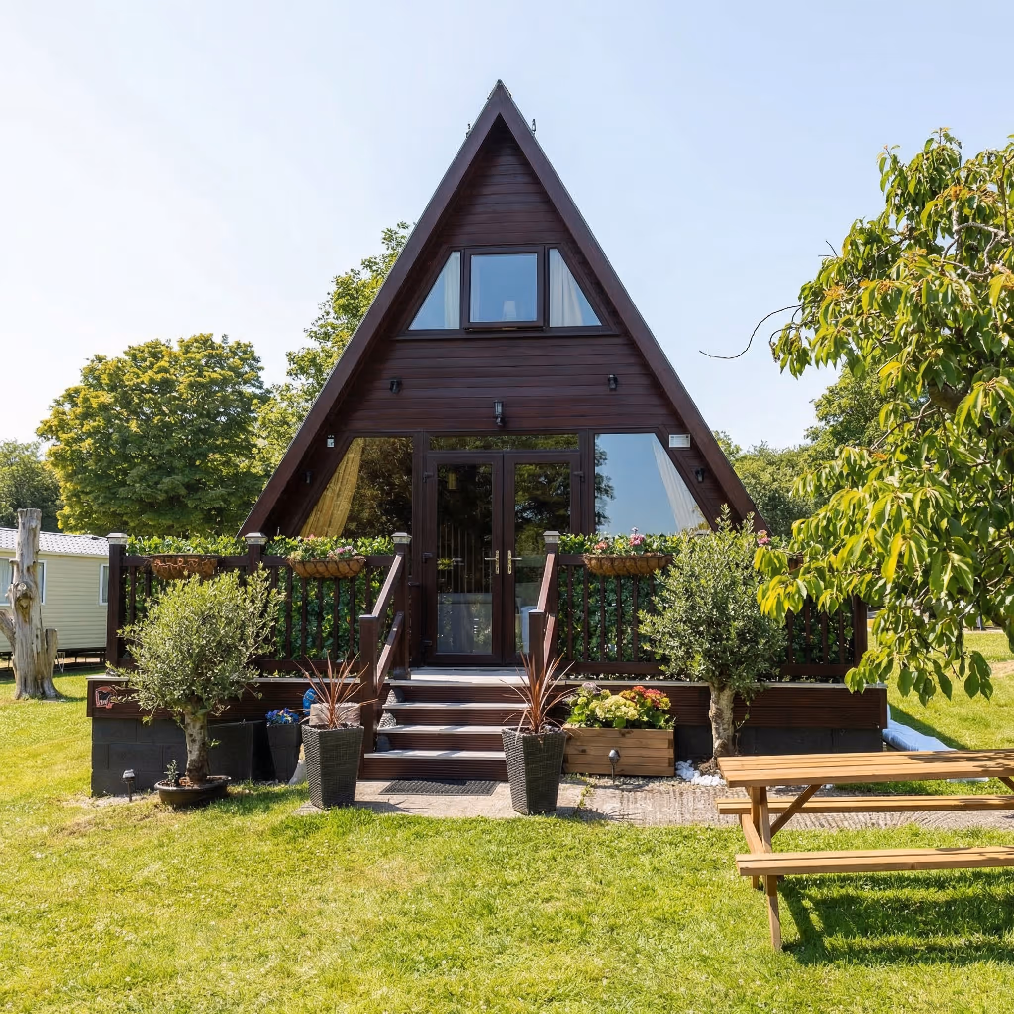 Front of Pops Cabin with its steps, planters and picnic bench on the lawn at Hafan y Môr