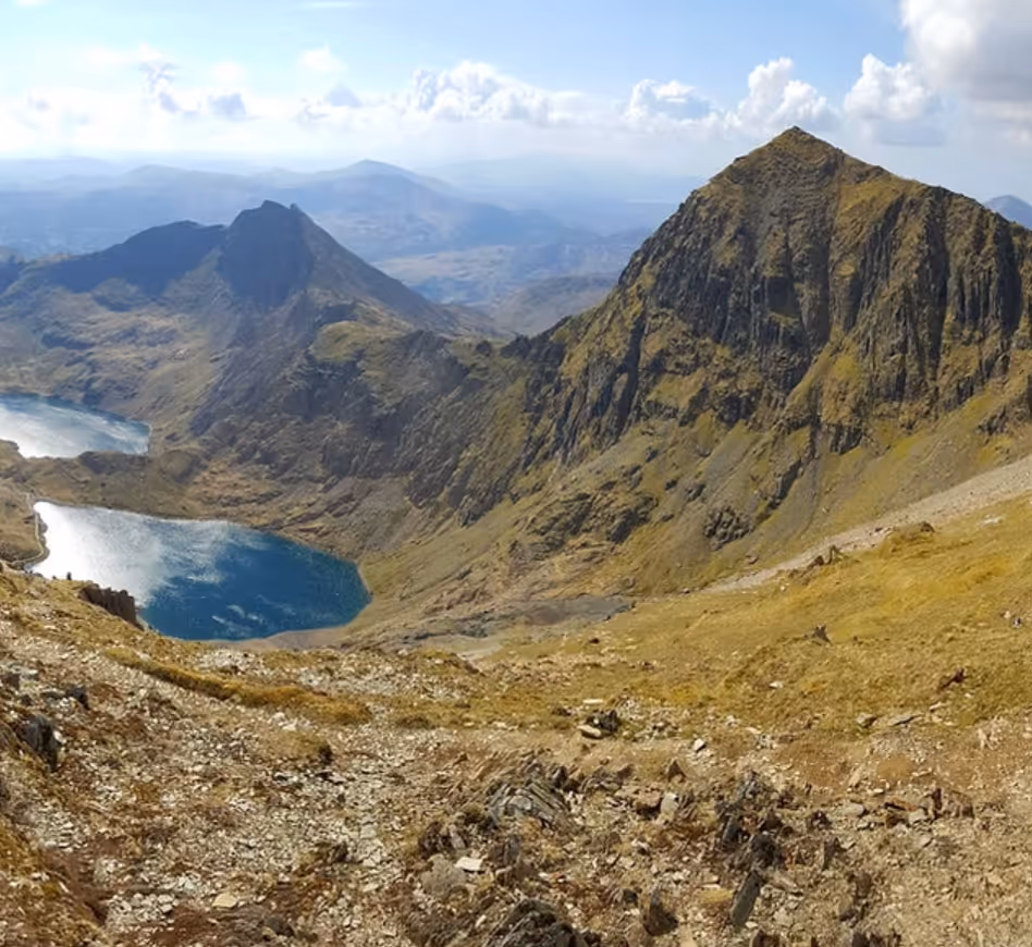 Rocky mountain landscape with two large lakes, clear sky, and distant mountain ranges.