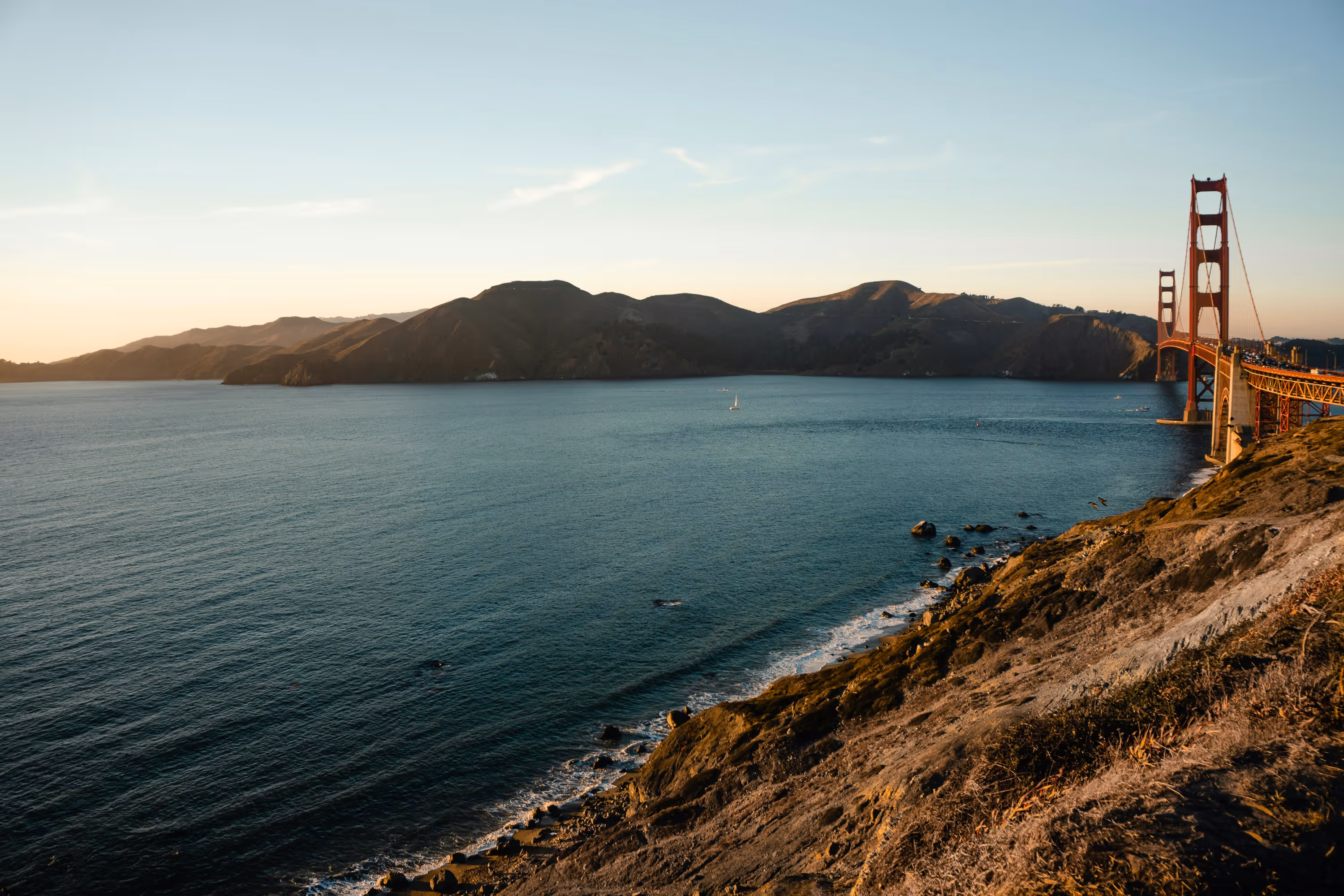 Golden Gate Bridge spanning across a bay with hills in the background during sunset.