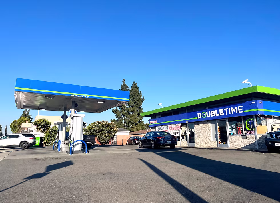 Gas station with blue and green canopy over pumps and a convenience store named Doubletime under clear blue sky.