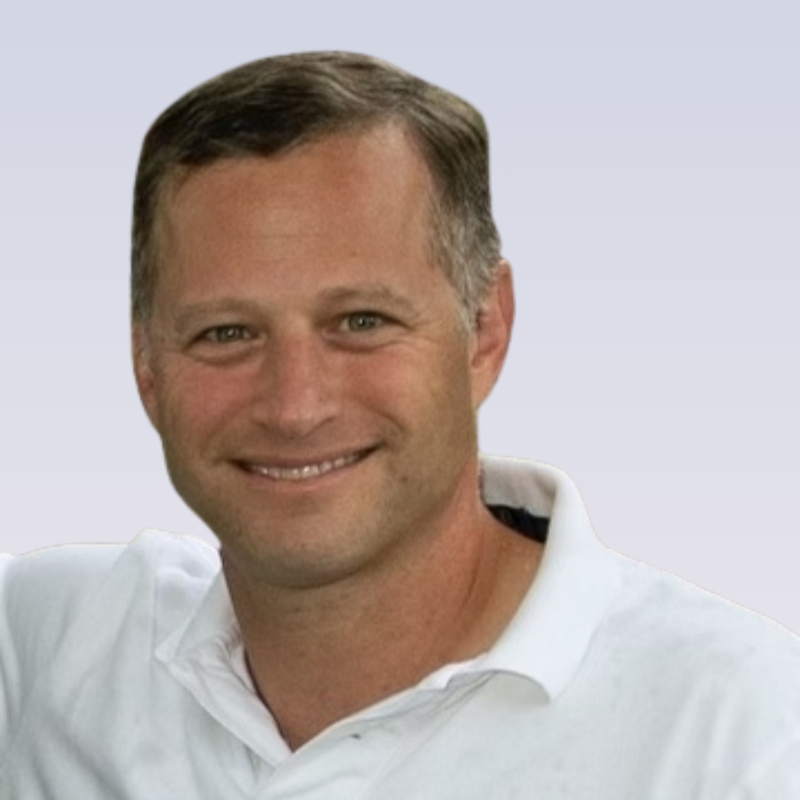 Smiling man with short brown hair wearing a white collared shirt against a light background.