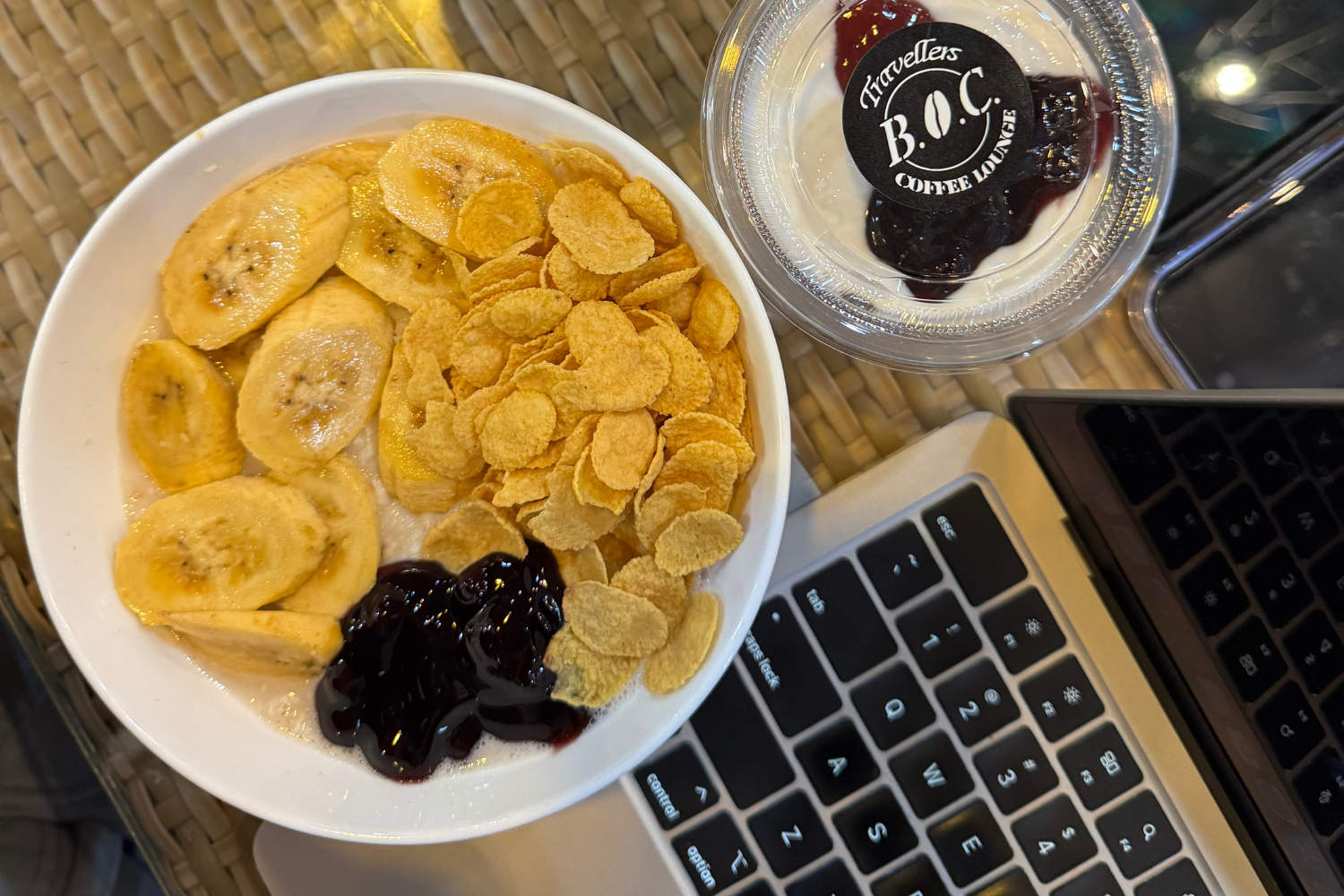 Digital nomad at an airport café with laptop open, balancing remote work while fueling up with food before boarding.