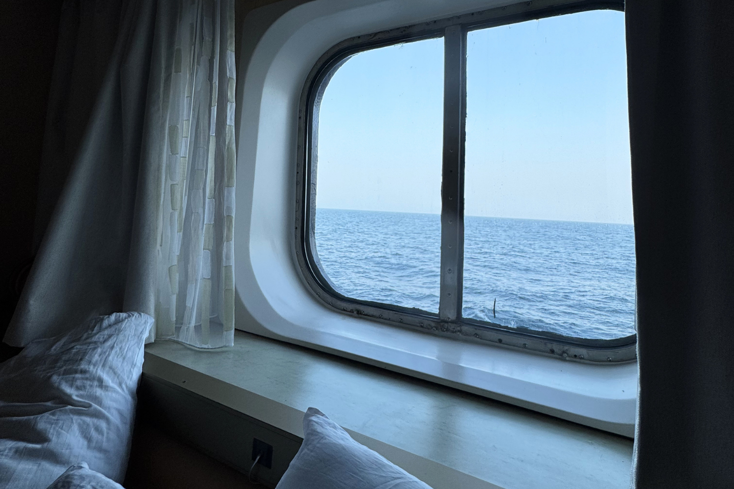Cruise ship cabin stateroom with bed beside window overlooking vast ocean