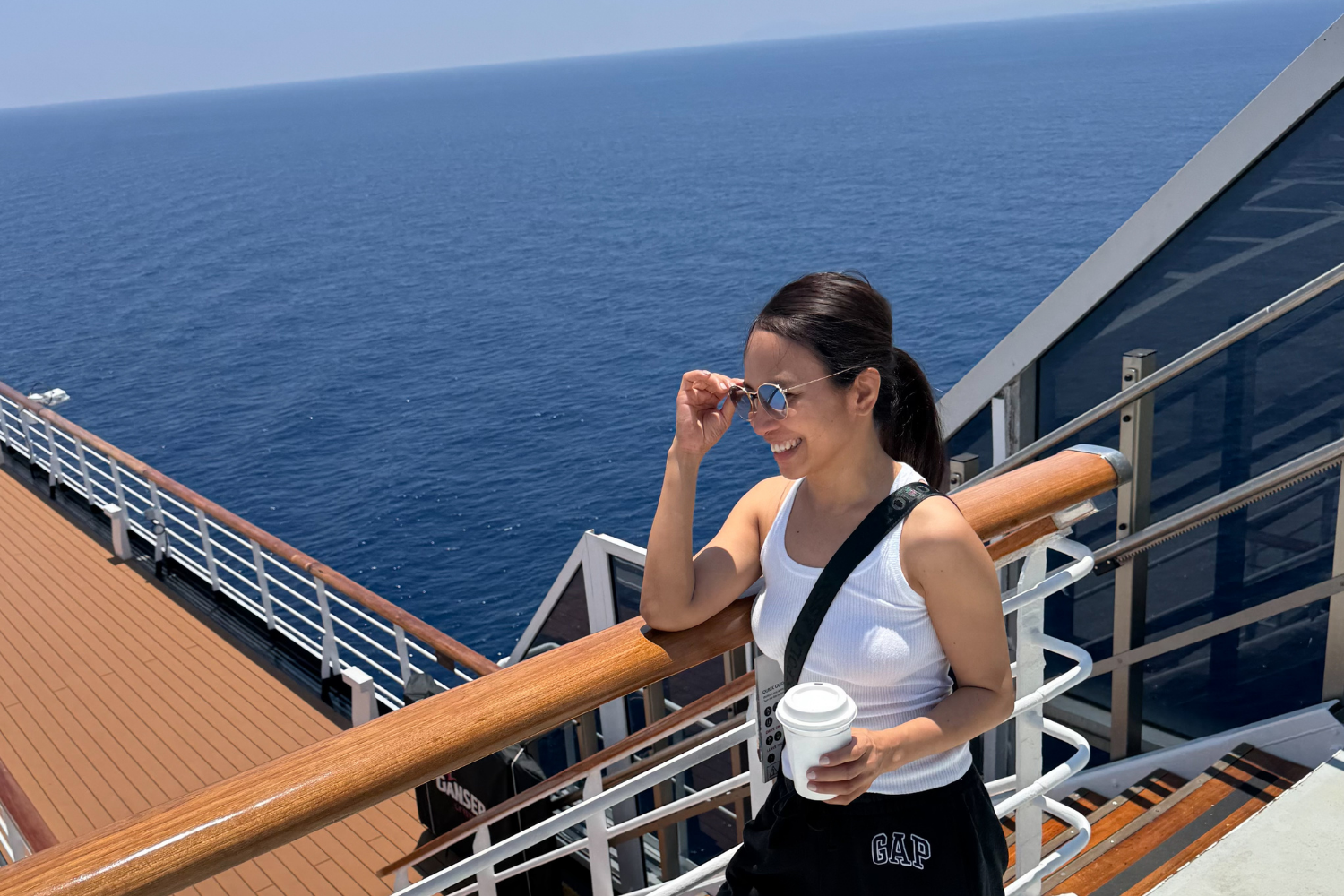 Woman on Deck 10 of cruise ship holding coffee with ocean view while sailing