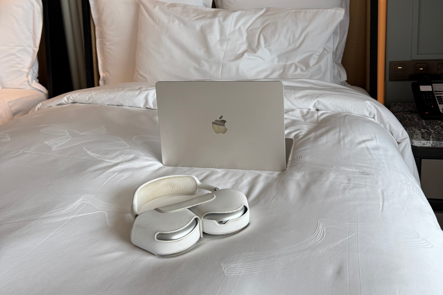 Laptop on hotel bed with AirPods Max at InterContinental Halong Bay Resort.