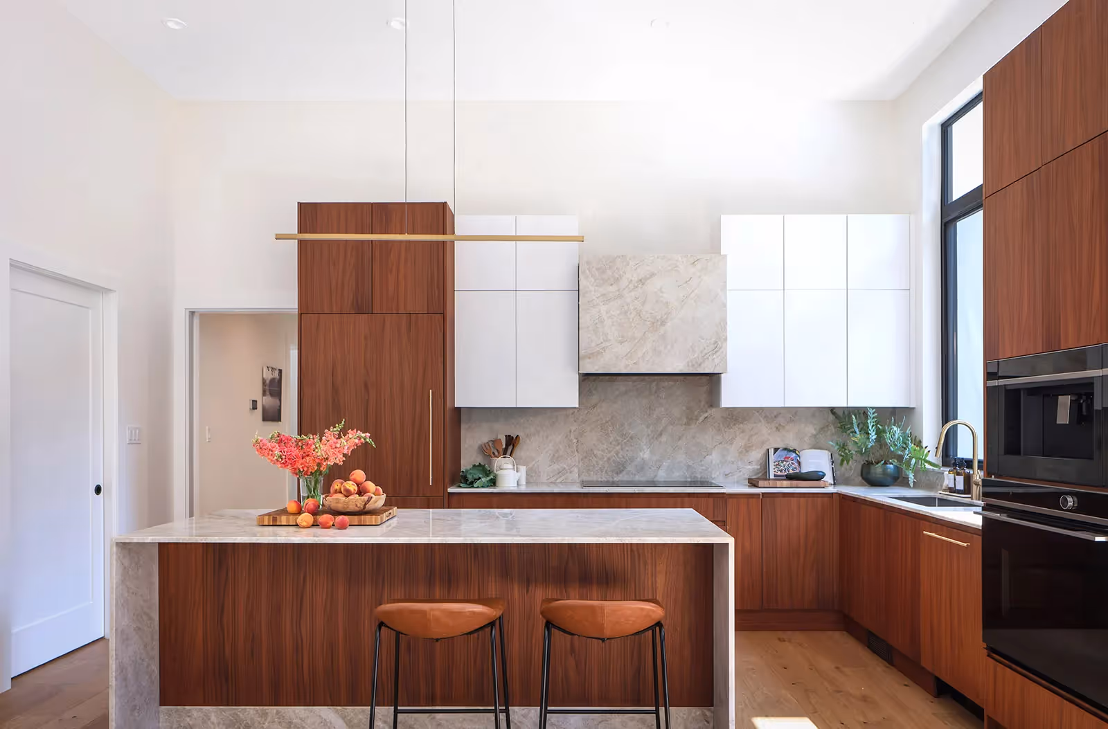 Luxury kitchen in Pine Forest home with waterfall marble countertop, rich wood cabinetry, and forest views
