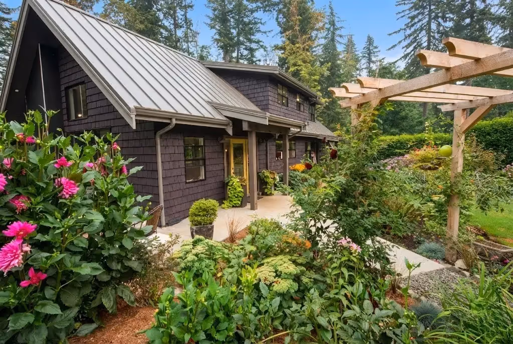 Garden of Eden renovation exterior with dark shingle siding contrasting vibrant curated garden on coastal Vancouver Island