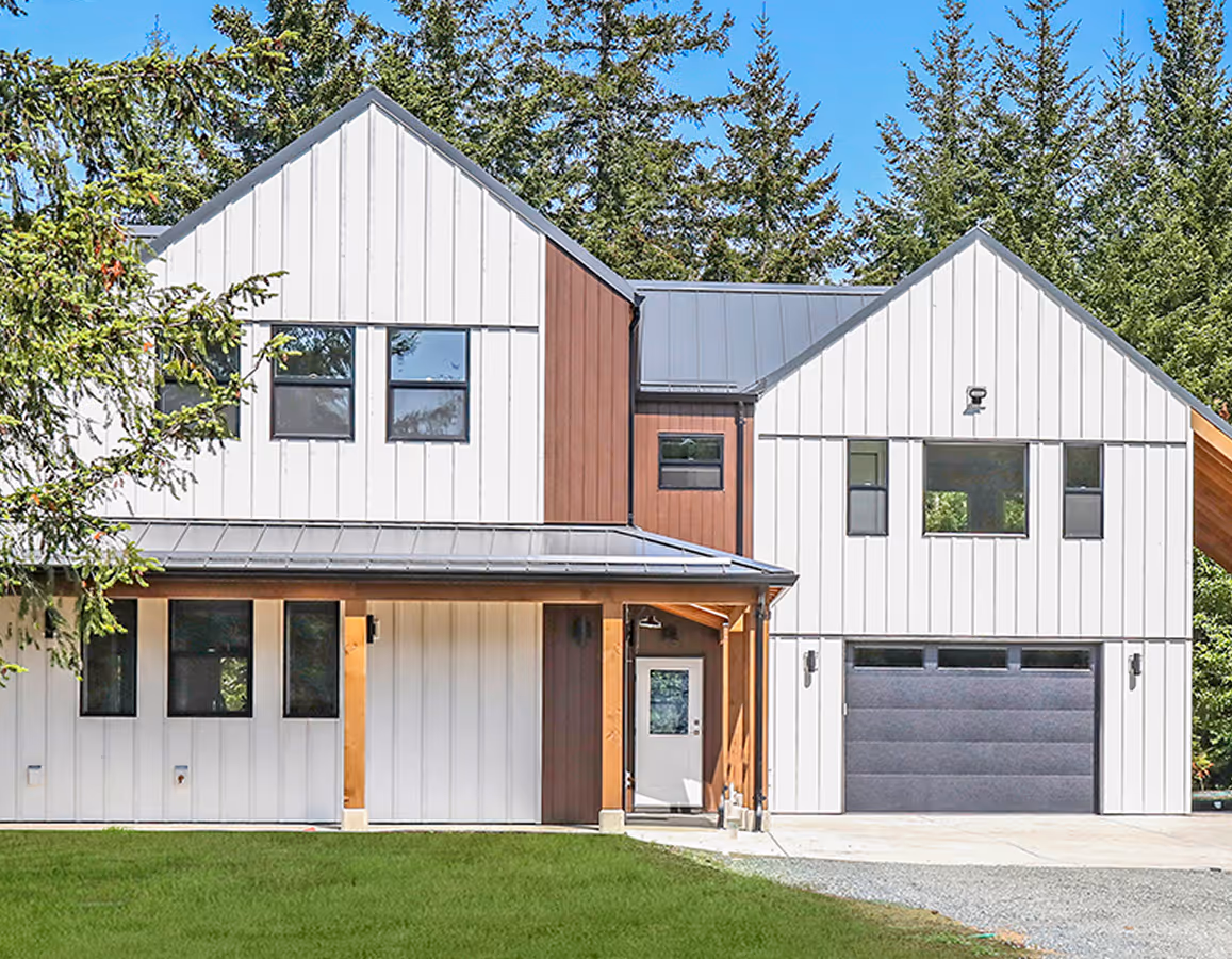 Sparrow Station modern farmhouse exterior with white board-and-batten siding, dark metal roof, and attached garage in Comox Valley
