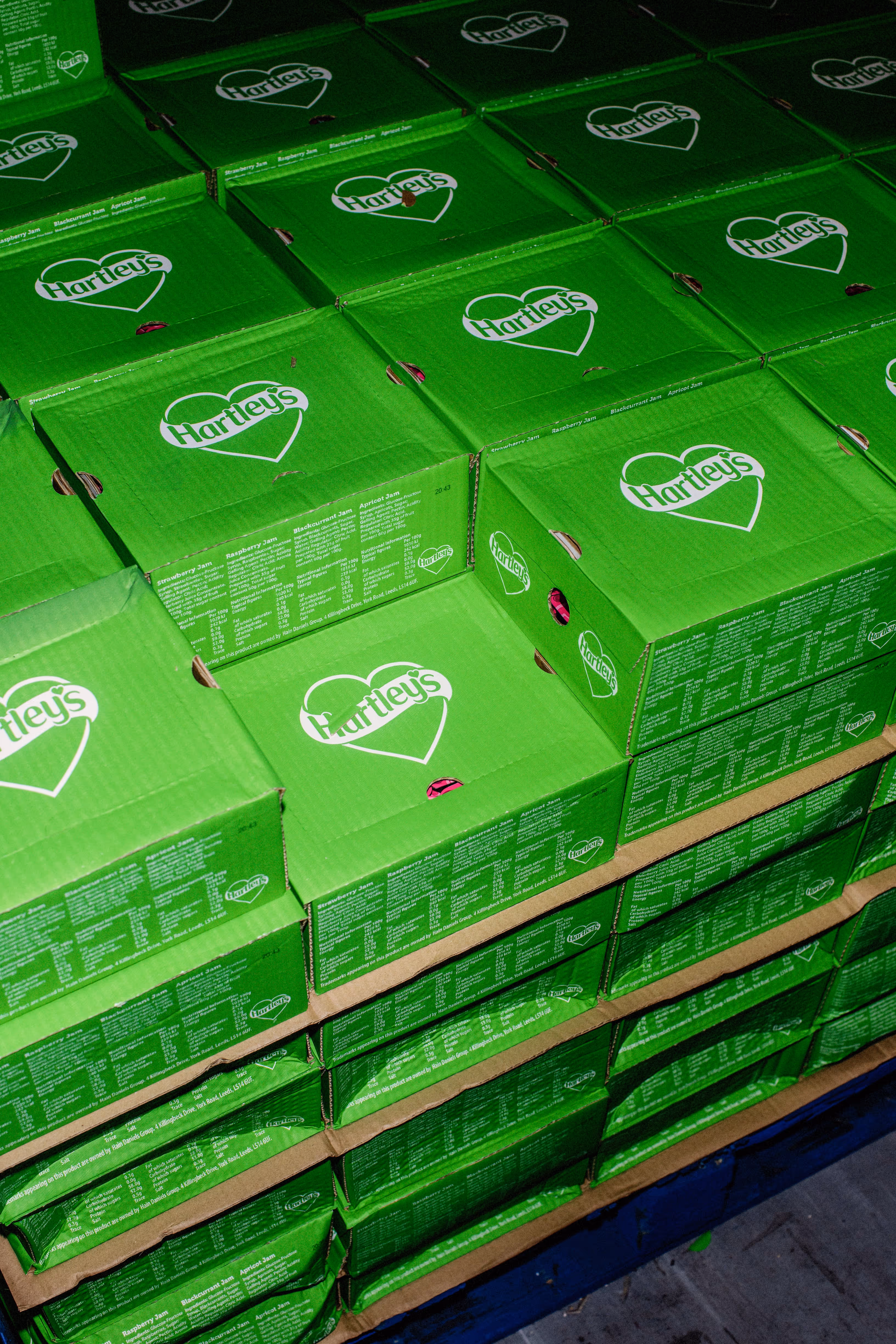 Stacks of green Hartley's jam boxes arranged on shelves in a warehouse.