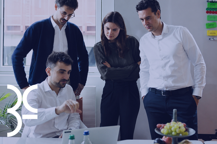 Four colleagues gathered around a laptop in an office, engaged in a discussion.