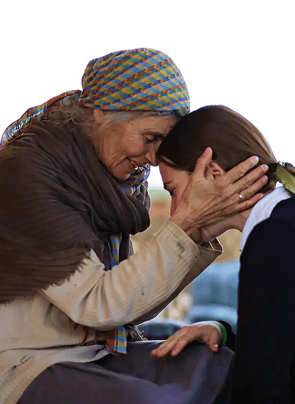 Elderly woman with colorful scarf embraces and comforts younger woman resting head on her.