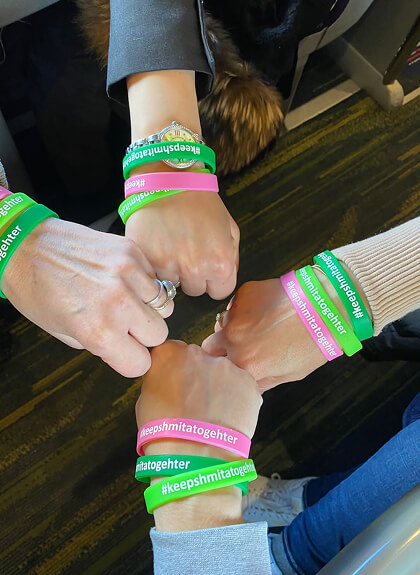 Four fists together each wearing green and pink wristbands with the hashtag #keepshmitatogether.