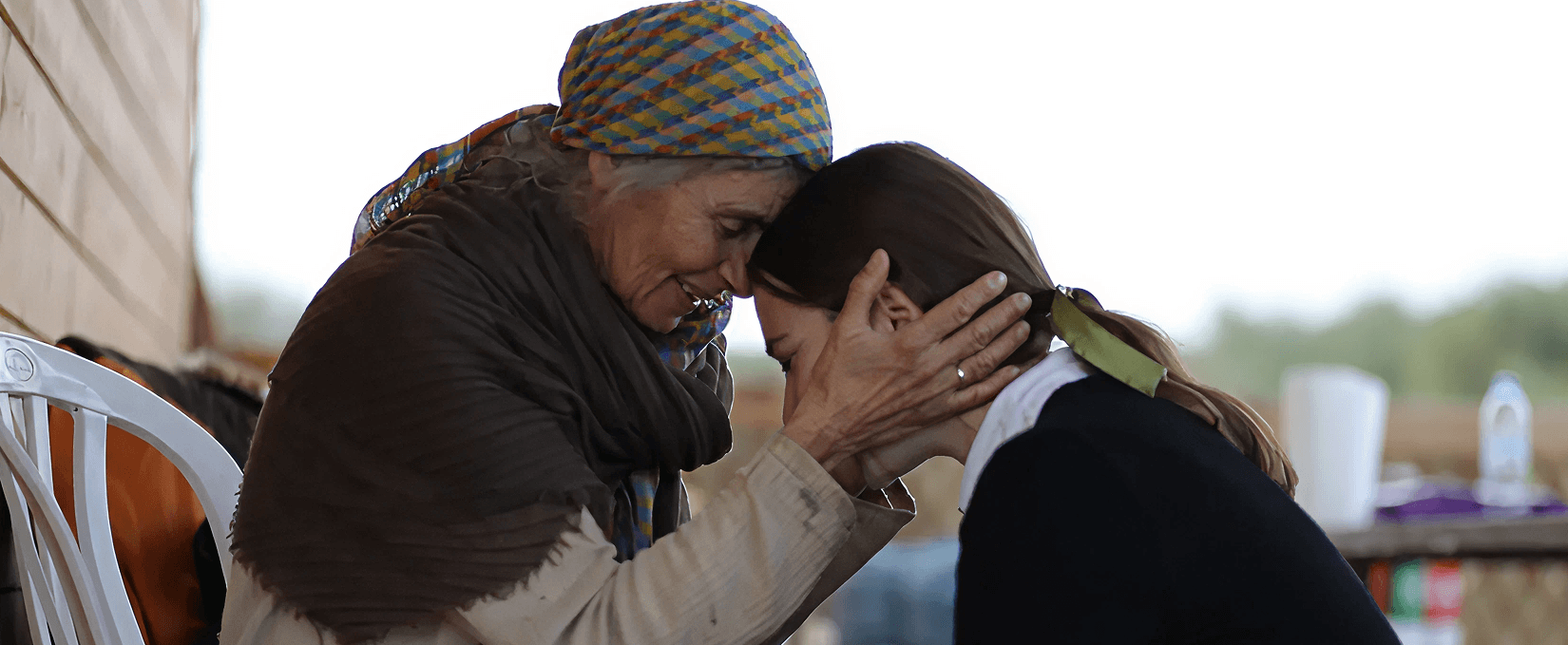 Elderly woman gently holds a younger woman's head, sharing a tender, close moment.