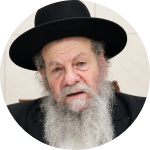 Elderly man with a long white beard wearing a black hat and black suit against a light background.