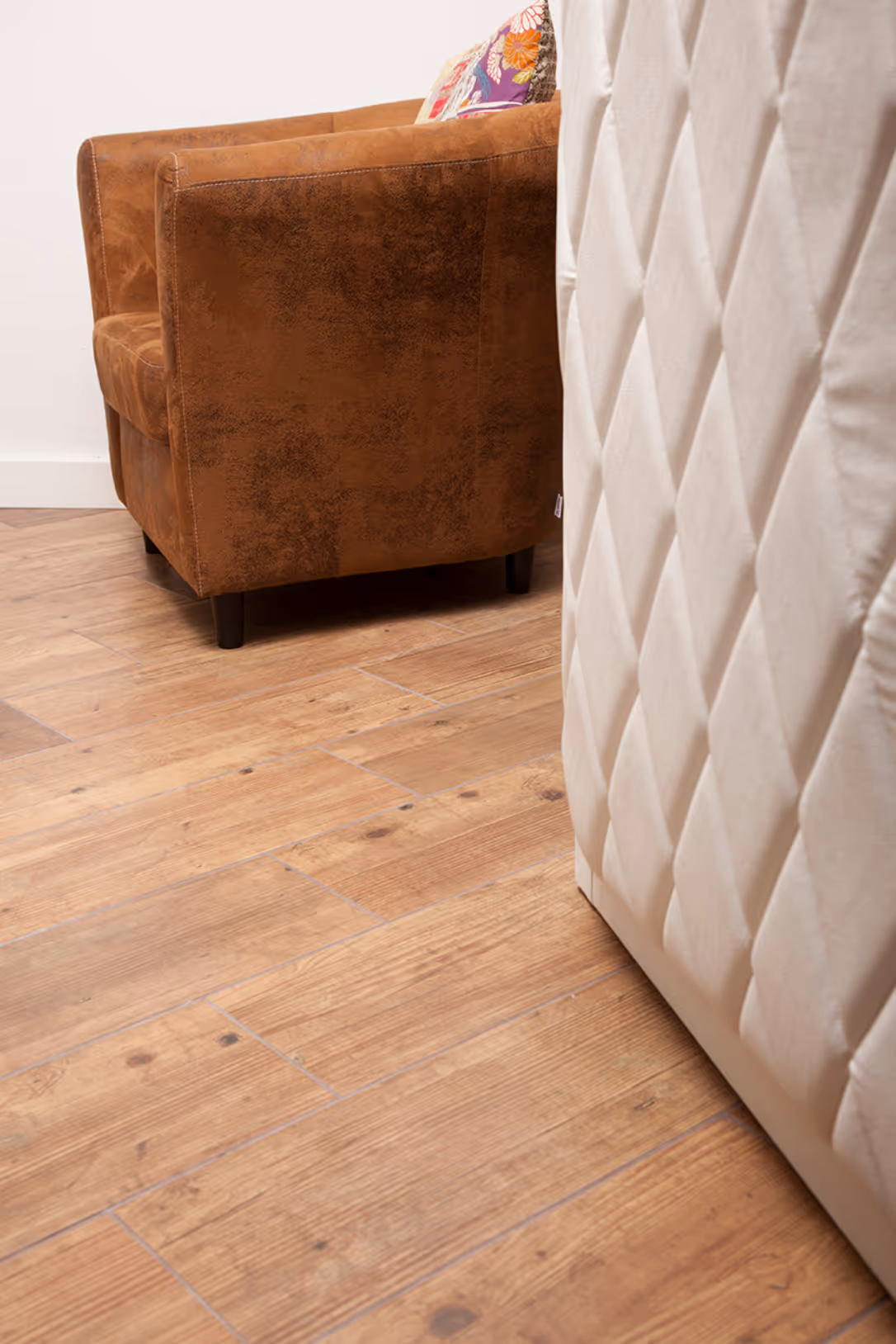 Brauner Sessel neben einem beigefarbenen, gesteppte Möbelstück auf Holzboden.