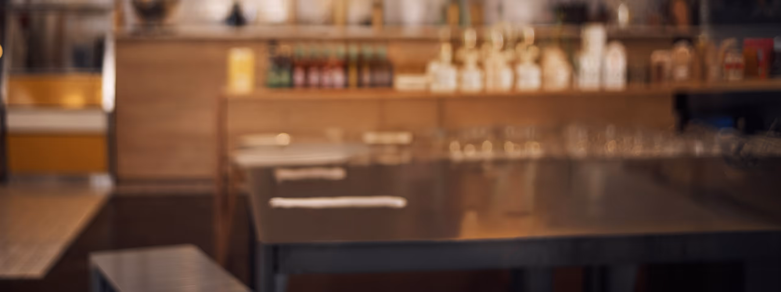 Blurred image of a modern coffee shop interior with wooden furniture and a counter in the background.