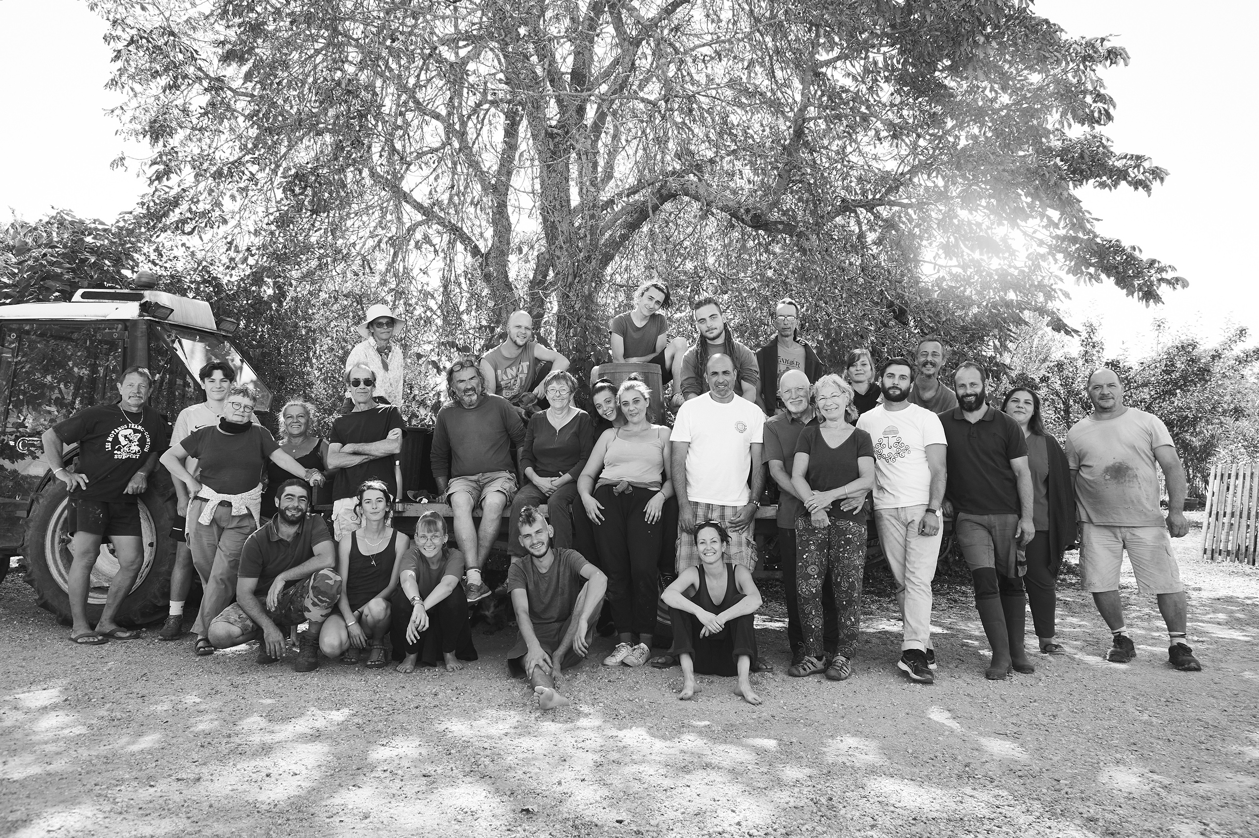 Groupe de 28 personnes posant devant un arbre et un tracteur en plein air par une journée ensoleillée.