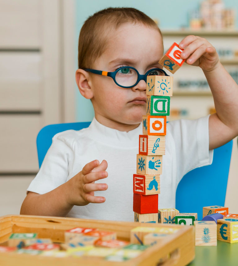 Young boy wearing glasses carefully stacking wooden alphabet blocks into a tall tower.