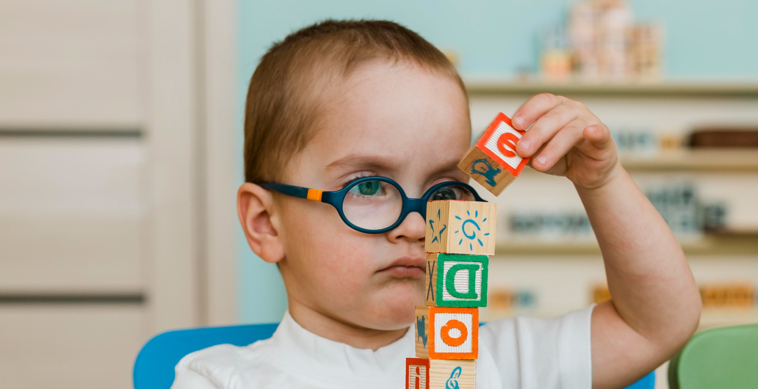 Young boy with round glasses focused on stacking colorful wooden blocks.