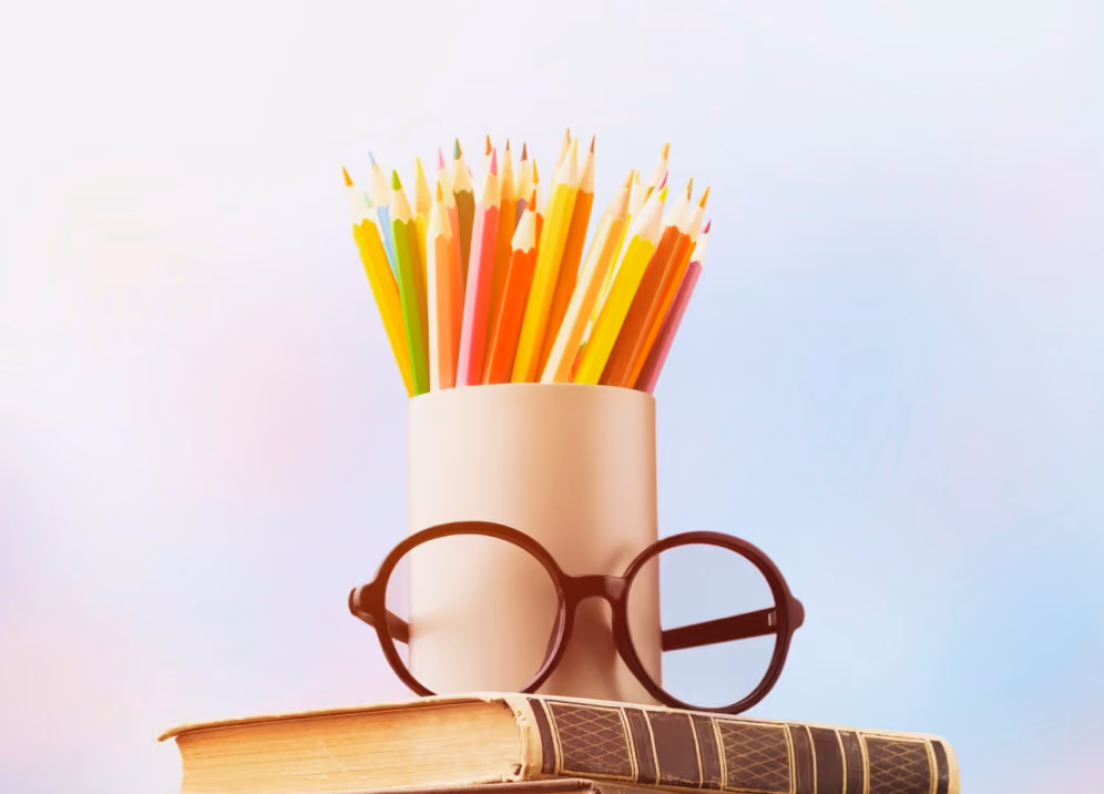 Black round glasses resting on two old books with a white cup holding colorful pencils behind them.